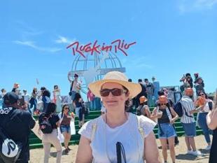 Fotografia da Associada Aida Fernandes no Rock in Rio Lisboa perto da estátua com o símbolo do Rock in Rio – um globo com uma guitarra, e por cima, a vermelho, as palavras Rock in Rio. 